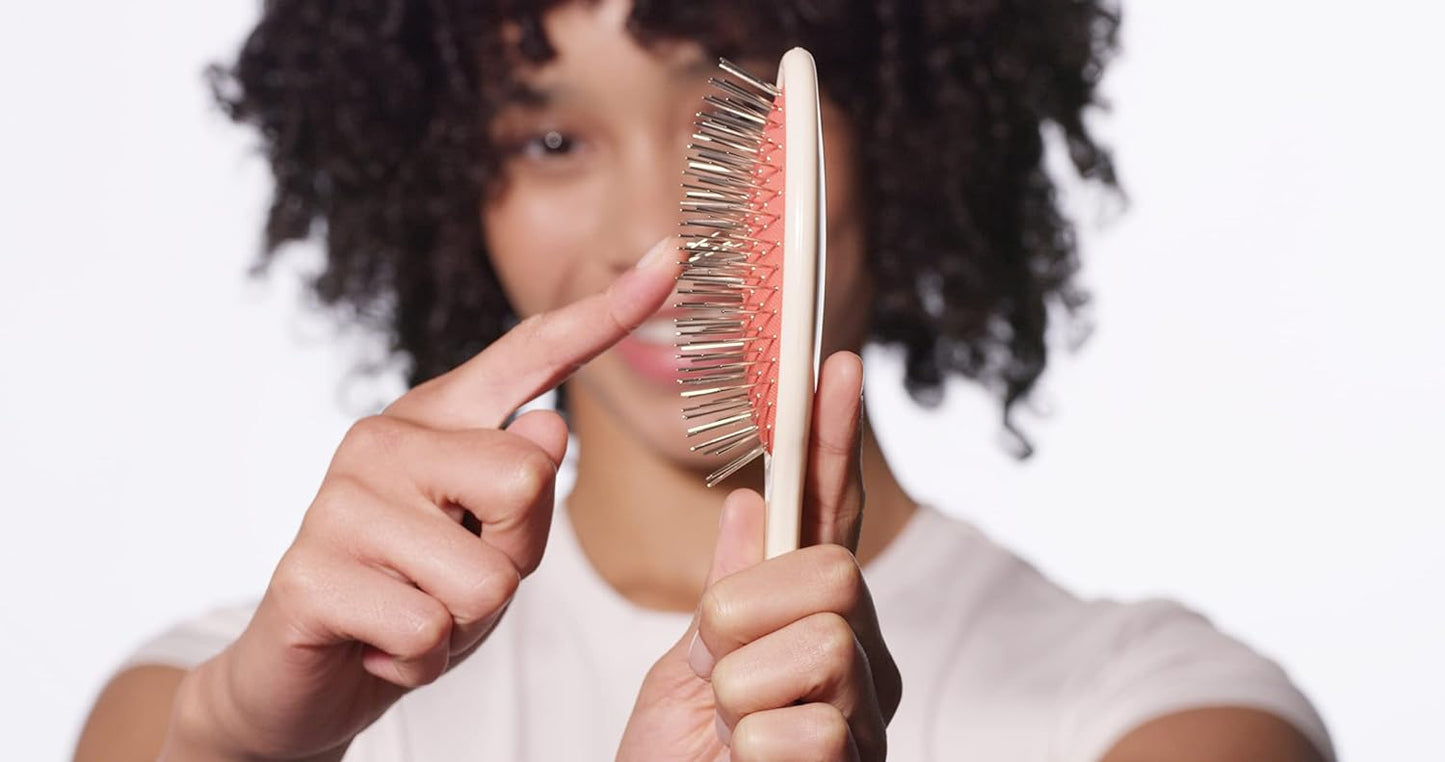 Woman gliding finger over metal bristles on the Untangle brush to show flexibility of brush. Bristles will not catch or snag on hair from flexible bristles.
